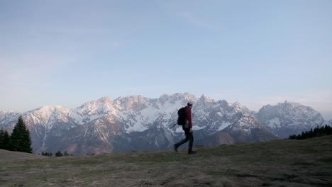 Un-Hombre-Con-Una-Mochila-Con-Un-Jersey-Rojo-Caminando-De-Izquierda-A-Derecha-Con-El-Parque-Nacional-Triglav-Y-Los-Alpes-Julianos-Al-Fondo