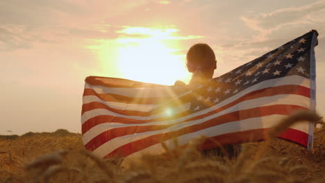 Frau-Mit-USA-Flagge-In-Den-Strahlen-Der-Untergehenden-Sonne-Steht-In-Einem-Weizenfeld