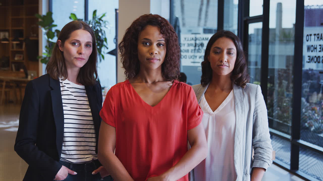 Retrato de três empresárias sérias de pé juntas em um escritório moderno de plano aberto.