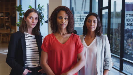 Portrait-Of-Three-Serious-Businesswomen-Standing-In-Modern-Open-Plan-Office-Together