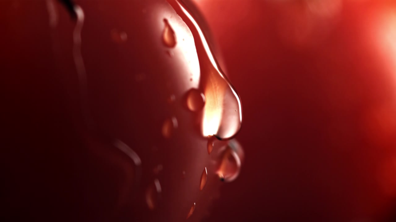 Primo piano di goccioline d'acqua che scivolano su un frutto rosso al rallentatore