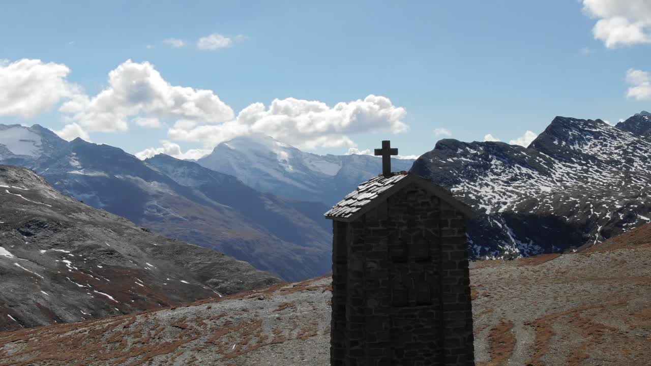 drone aéreo dando vueltas alrededor del campanario de una pequeña iglesia de piedra con un paisaje montañoso en el fondo, col de l'iseran, francia