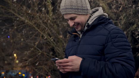 Close-up-portrait-of-excited-smiley-young-man-texting-on-smartphone-outdoor
