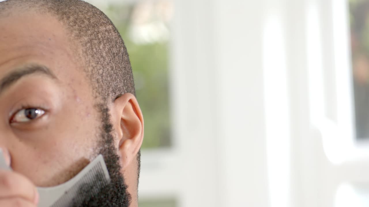 Video verticale: Uomo in camicia chiara che appoggia il pettine vicino al naso, pettinando e modellando il bordo della barba vicino alla finestra.