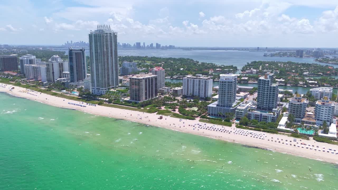 Turquoise ocean of Miami Beach, hotels on white sand beach with downtown Miami skyline in background, Florida. Aerial drone orbiting