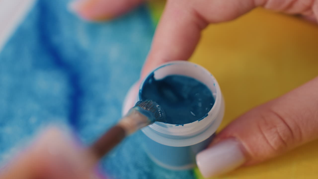 Primer plano de unas manos caucásicas mezclando pintura verde azulado en un bote, con manicura visible, fondo de toalla suave de estudio, trazos lentos y deliberados, textura de pigmento brillante, ambiente tranquilo y concentrado, proceso creativo capturado