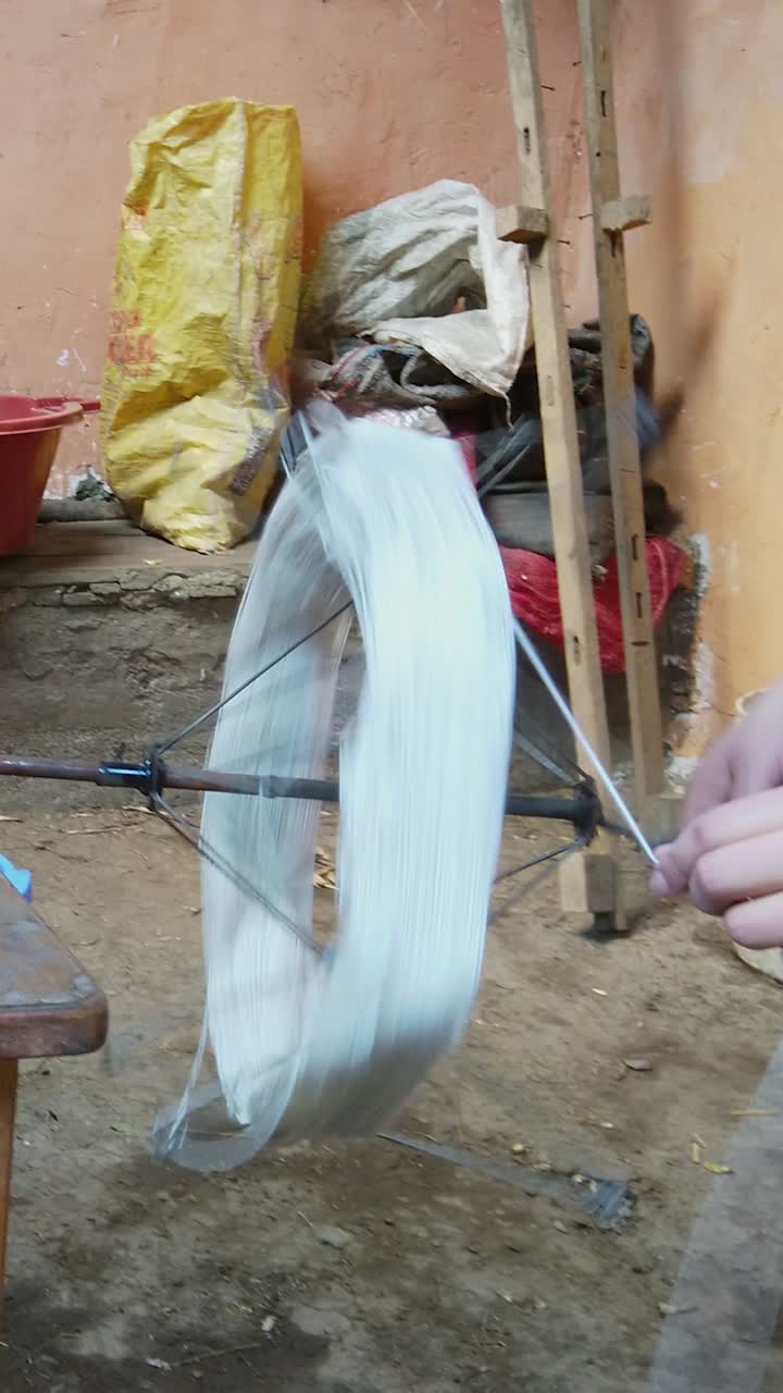 White wool being hand spun with manual swift, close up of person hands turning handle in rustic indoor setting near Cusco. Vertical shot
