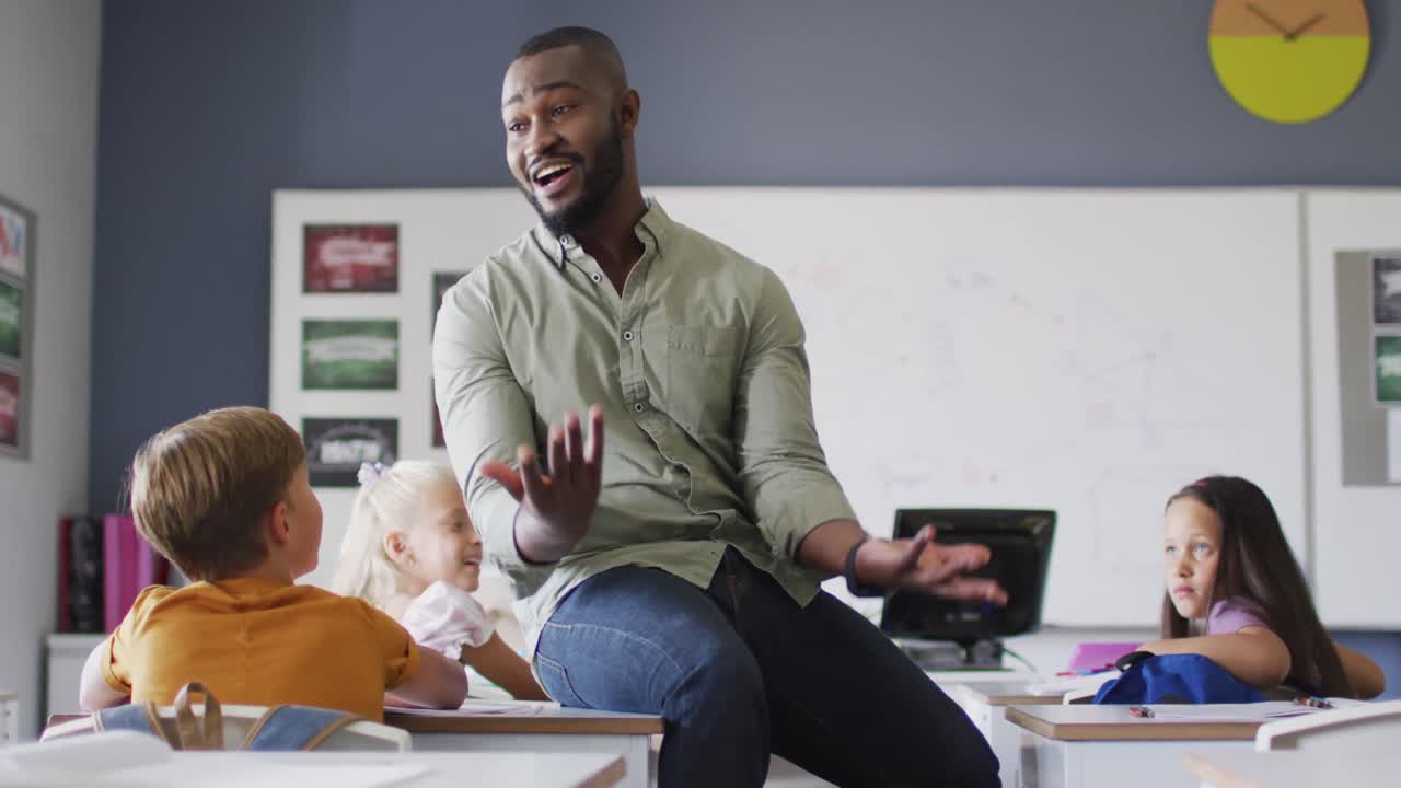 Video of happy african american male teacher during lesson with class of diverse pupils