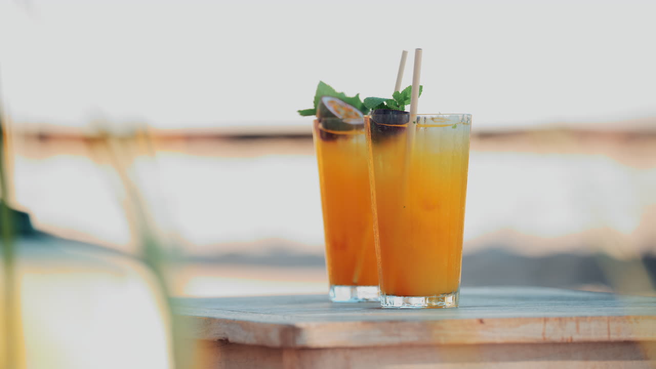 Two bright orange cocktails with mint and passion fruit on a small wooden table at a beach club
