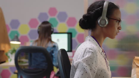 jovem mulher de negócios de raça mista usando computador navegando on-line trabalhando em um projeto de rede ouvindo música desfrutando de escritório de startup na moda verificando smartphone