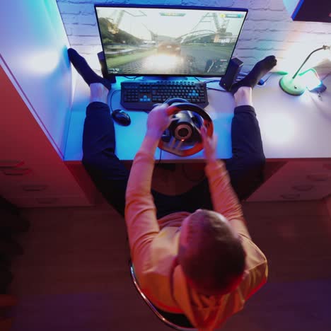 man is playing game on computer at home. male gamer enjoying car racing video game with steering wheel. gaming concept. top view.