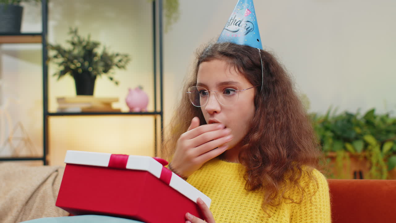 glückliches teenager-kind hält geburtstagsgeschenk-box mit band feiern party eröffnung geschenk zu hause