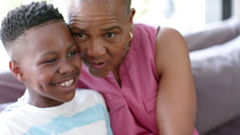 happy african american grandson and grandmother talking and embracing on sofa, slow motion