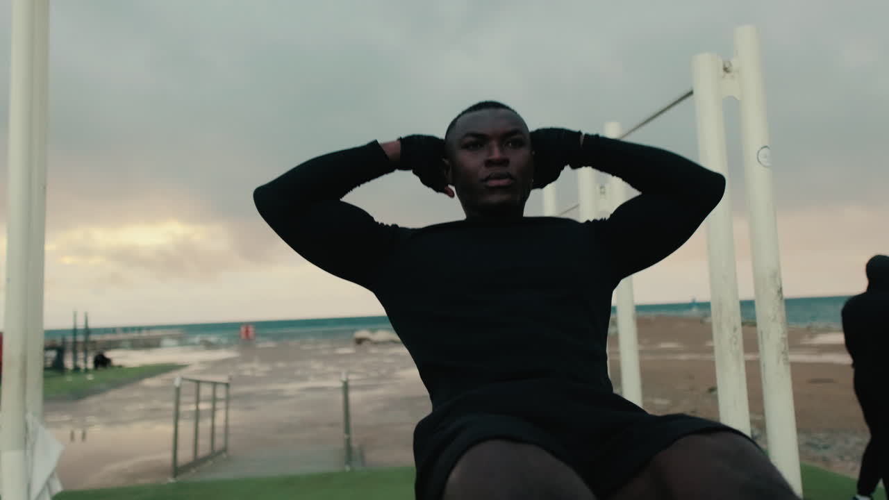 Young Man Doing Sit-ups on Outdoor Exercise Equipment by the Beach