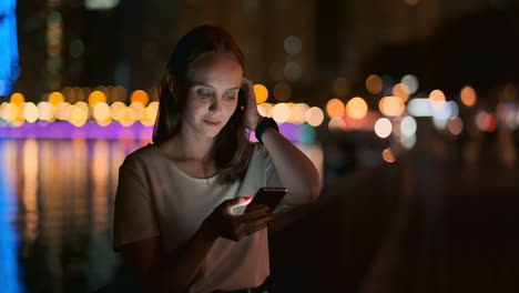 Ein-Schönes-Junges-Mädchen-Im-Sommer-In-Einer-Großen-Nachtstadt-Hält-Ein-Smartphone-In-Der-Hülle-Und-Schreibt-Eine-Nachricht,-Liest-E-Mails-Und-Kommuniziert-In-Chatrooms-Und-Sozialen-Netzwerken,-Führt-Einen-Blog-Und-Schaut-Auf-Den-Telefonbildschirm