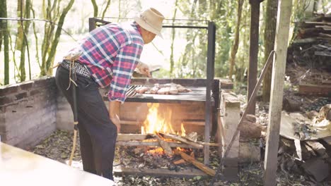 ethnic man preparing raw meat pieces above burning fire