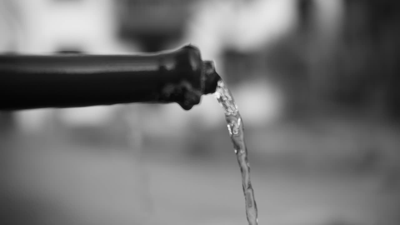Filmato in Bianco e Nero di Acqua che Scorre da un Tubo con uno Sfondo Sfocato, che Cattura un Aspetto Artistico e Astratto