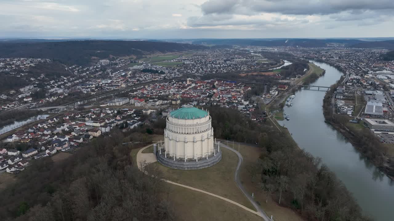 Drone shot of the majestic Befreiungshalle in Kelheim, Germany, perched atop a hill overlooking the Danube River and surrounding landscape on a cloudy day