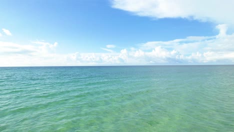 Drone-flying-low-over-white-sand-beach-and-clear-emerald-waters-on-a-summer-day-with-fluffy-clouds-in-the-sky-on-the-Gulf-of-Mexico-Pensacola-Florida