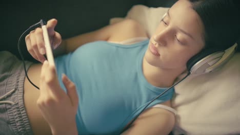 teen girl relaxing at home, listening to music with headphones and using her smartphone. a calm, intimate moment of digital leisure in a cozy setting.