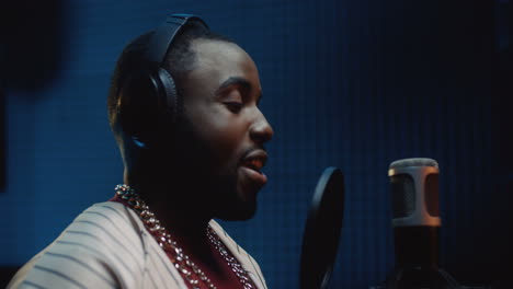 attractive smiled and stylish r'n'b or blues male singer recording a vocal in the sound studio while singing in the microphone