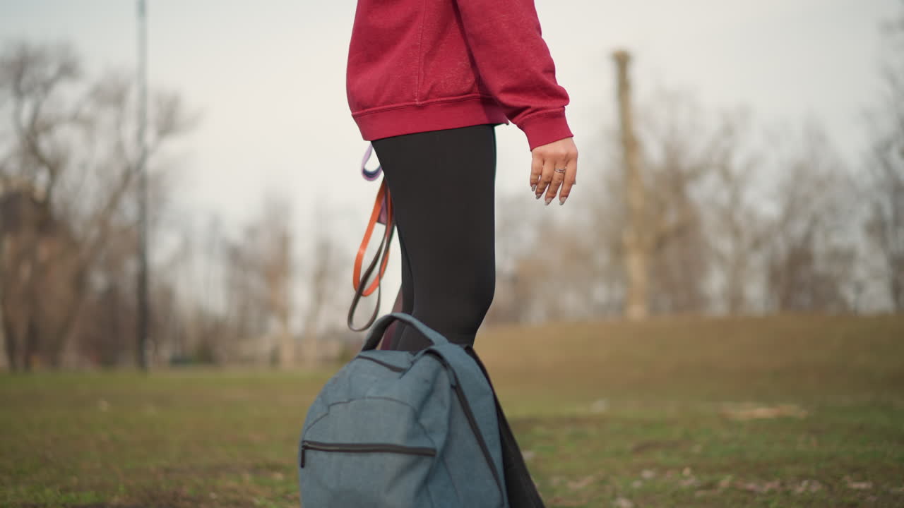 Asian Woman Walking In Park CloseUp On Legs And Hands Holding Backpack And Colorful Leashes, Leggings And Sneakers Visible, Emphasis On Movement, Kit And Readiness For Active Outdoor Session