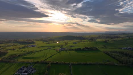 flying over farmland of english countryside towards setting sun at golden hour