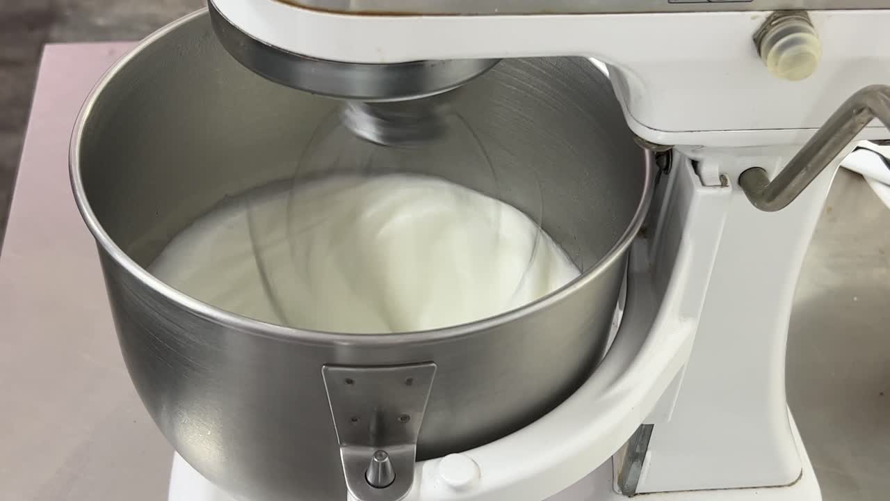 Commercial kitchen setting close up shot of a heavy duty electric mixer mixing egg white and sugar until it is glossy peak and stiff peak, preparing meringue buttercream
