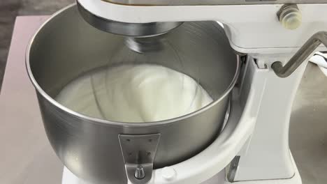 commercial kitchen setting close up shot of a heavy duty electric mixer mixing egg white and sugar until it is glossy peak and stiff peak, preparing meringue buttercream