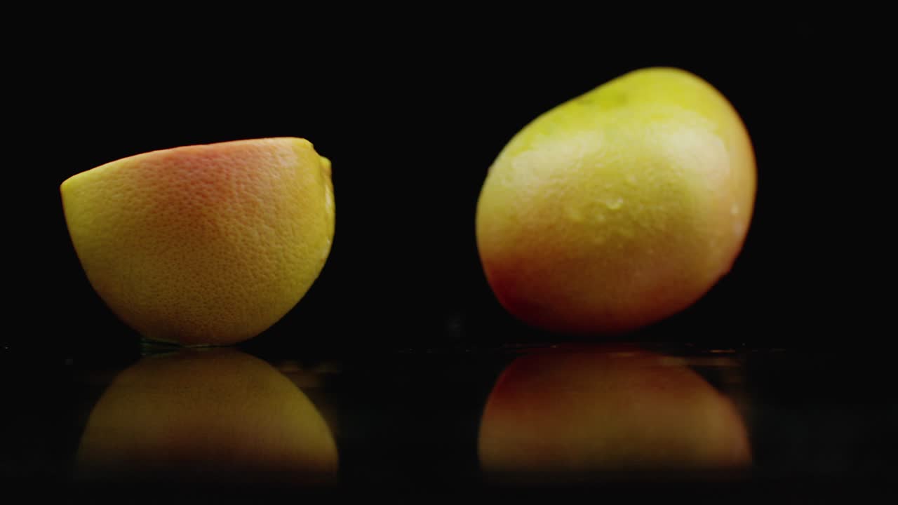 cámara lenta. pomelo jugoso con gotas y se rompe en 2 rebanadas con salpicaduras en una mesa de vidrio con reflexión en un fondo oscuro