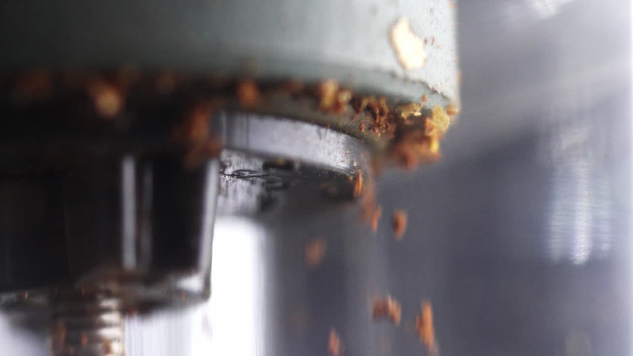 Slow motion footage of coffee grounds falling from a metal grinder in a kitchen or café setting, highlighting texture, precision, craftsmanship and the coffee making process