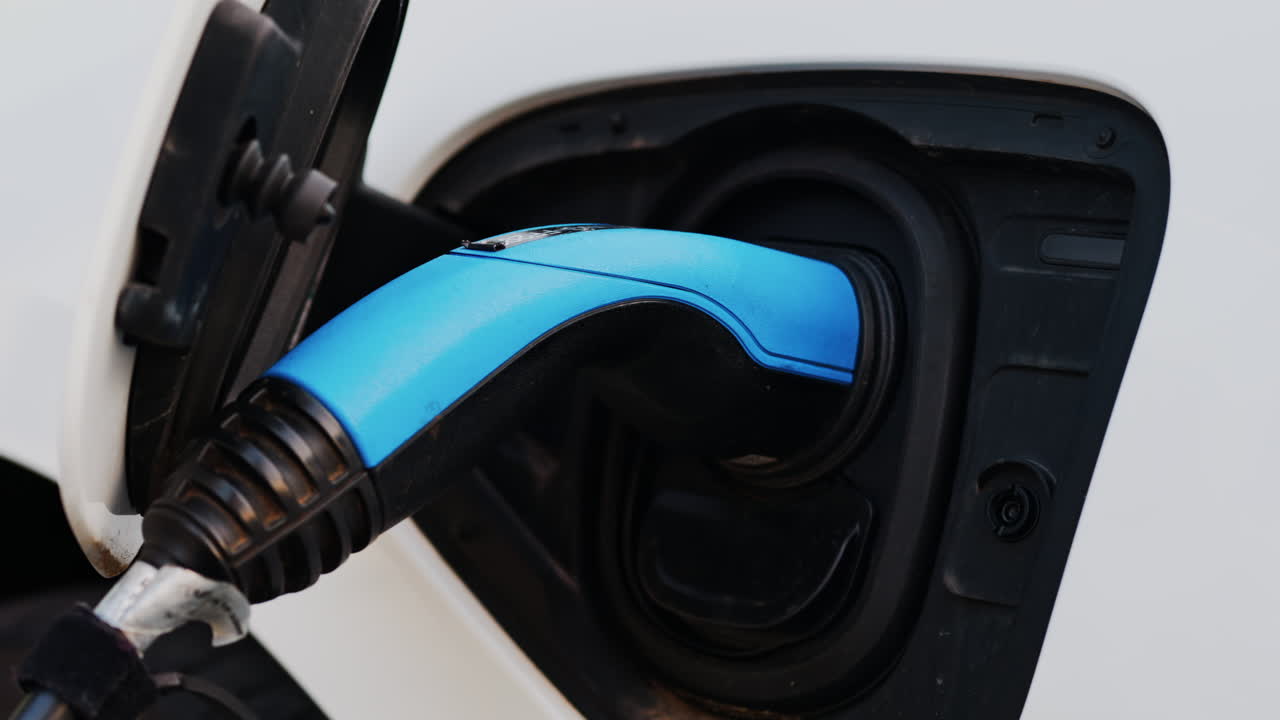 Beyaz bir arabaya takılı mavi bir elektrikli araba şarj cihazının yakın çekimi