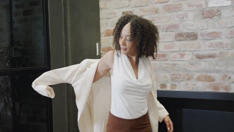 Portrait-of-happy-biracial-businesswoman-putting-on-jacket-and-smiling-to-camera,-slow-motion