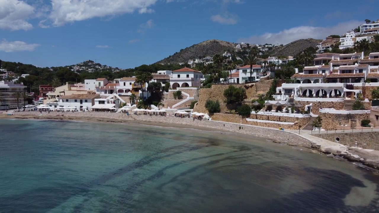 Ripresa con drone che rivela la suggestiva insenatura della spiaggia di El Portet a Moraira, Alicante. Vista aerea delle acque turchesi del Mediterraneo, della costa idilliaca e delle ville di lusso in collina in Spagna.