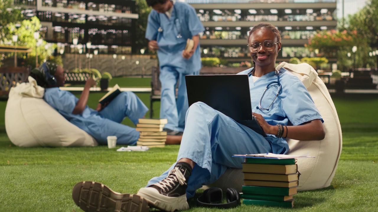 Portrait of woman student smiling and typing on laptop seated on beanbag
