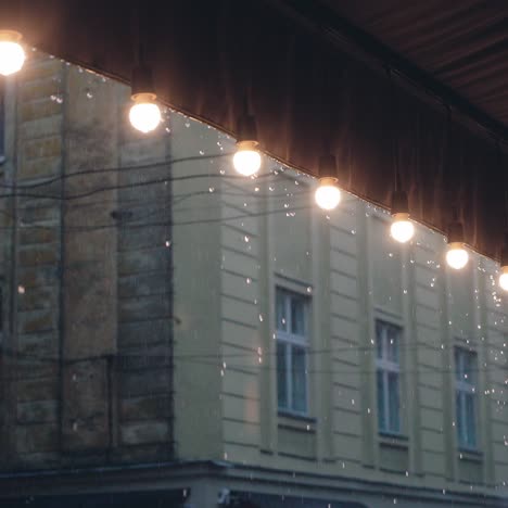 raindrops are falling on the roof of the restaurant with a decorative row of lamps on the background of building. it is raining
