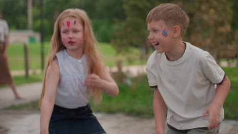 playful kids in park throwing stones, grimacing with pained faces, blurred adults watching nearby, tension visible as small group engages in risky game, summer greenery background