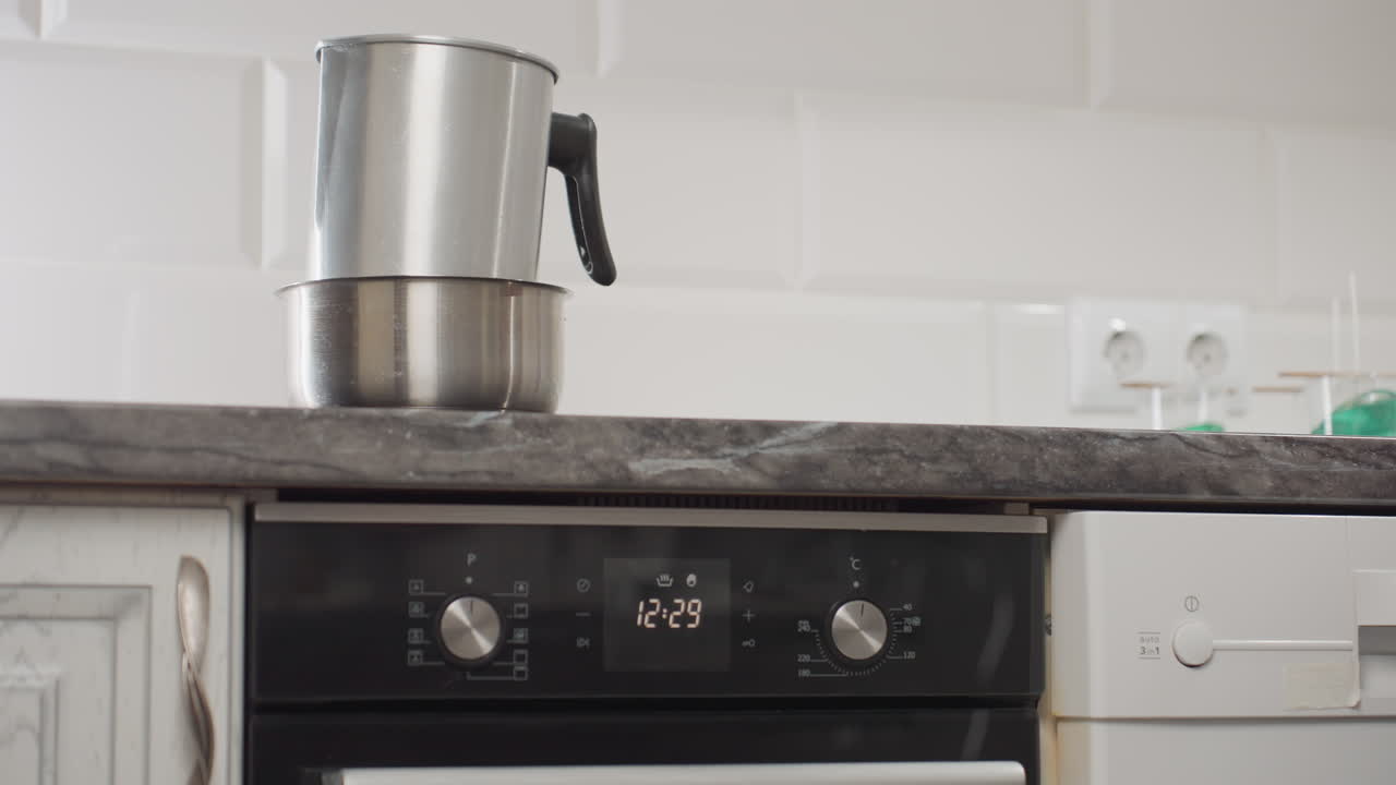 Beautiful lady in long gown wearing bracelets walks toward kitchen workspace to switch on table gas as pot with dish sits on countertop, capturing domestic routine, stylish presence, and cooking preparation process