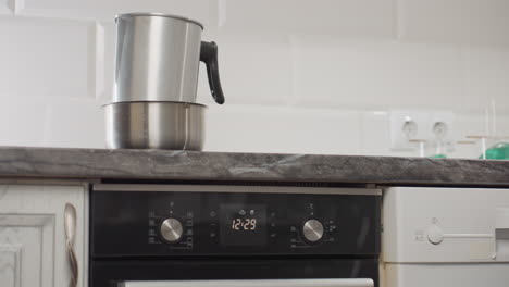 beautiful lady in long gown wearing bracelets walks toward kitchen workspace to switch on table gas as pot with dish sits on countertop, capturing domestic routine, stylish presence, and cooking preparation process