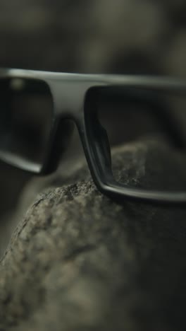 glasses resting on a rock with a blurred background, focusing on their details