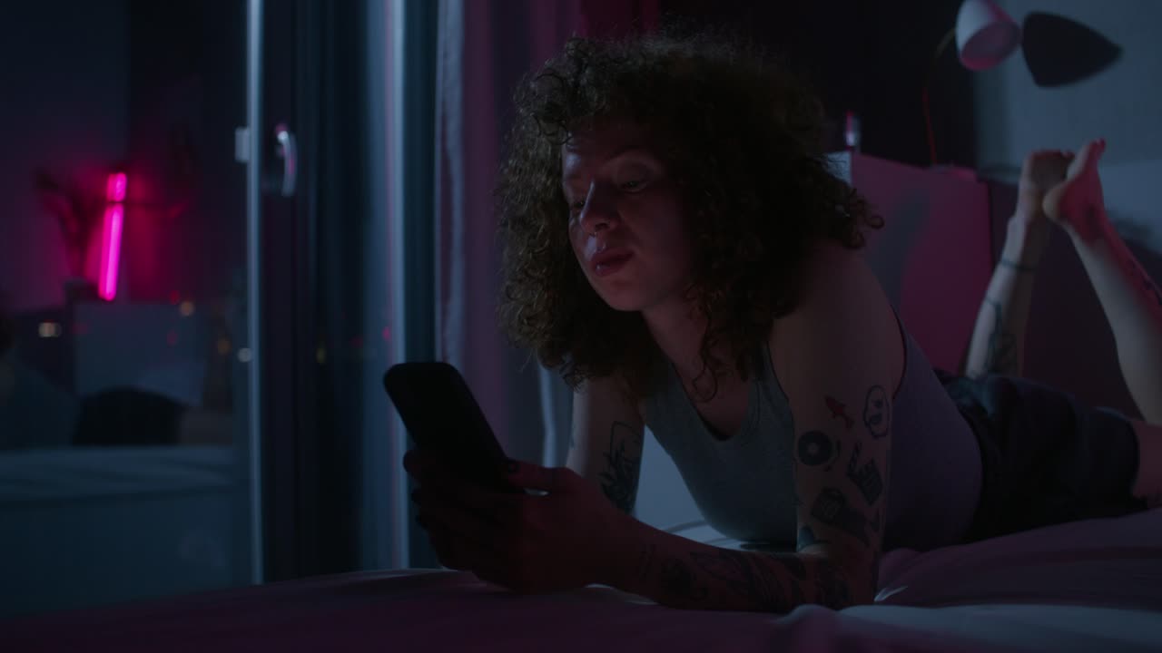 mujer joven relajándose en el dormitorio por la noche usando el teléfono móvil