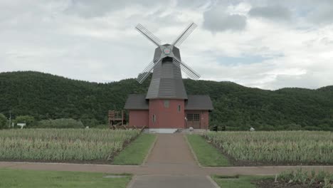 Man-Running-on-Narrow-Road,-Dutch-Windmill-and-Mountain-Silhouette-Background