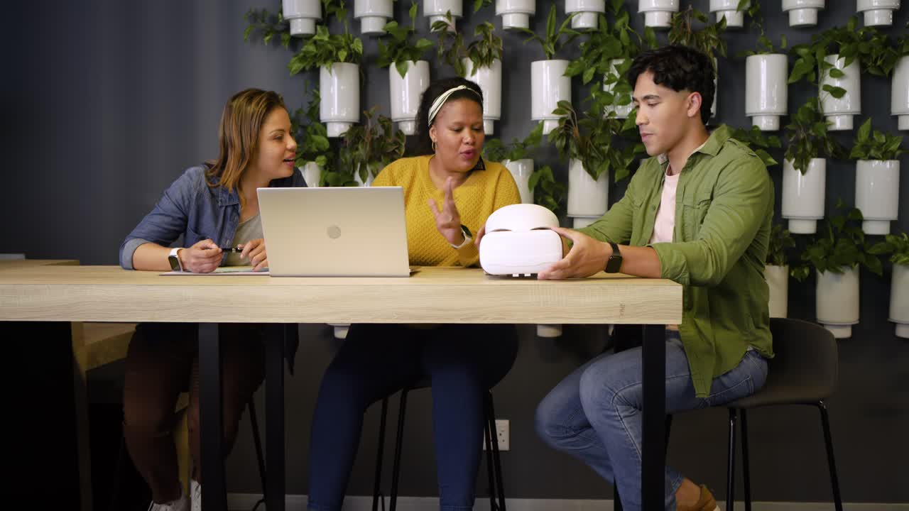 Diverse colleagues laughing after joke then examining VR headset for user feedback at office nook
