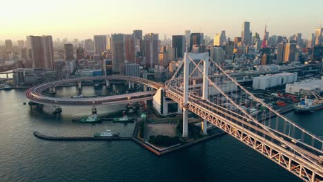 Toma-Aérea-De-Drones-Del-Circuito-Del-Tren-Cerca-Del-Puente-Colgante-Del-Arco-Iris-En-La-Ciudad-De-Odaiba,-Tokio,-Japón,-Con-La-Torre-De-Tokio-En-El-Fondo