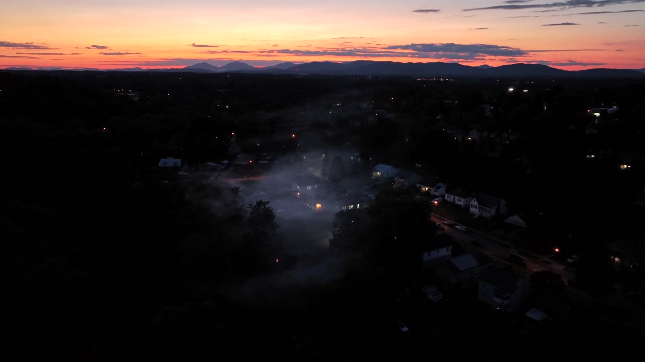 Dense fog between apartment houses in quiet suburb district of town. Aerial approaching shot. Quiet dawn scene with colored sunrise. American city suburb in USA. Landing shot.Mystic scene with lantern