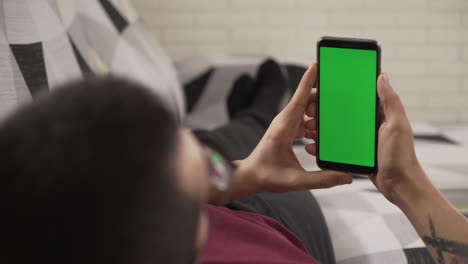 joven tendido en el sofá mirando su teléfono celular, pantalla verde