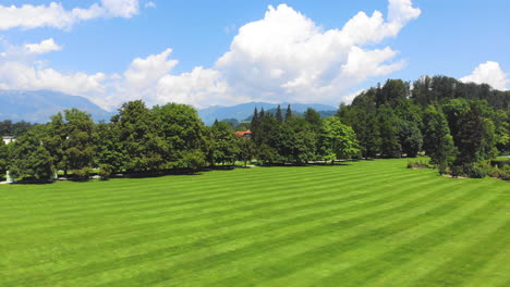 medium wide angle dolly in drone shot of well maintained lawn and surrounding trees in volcji potok arboretum during the day