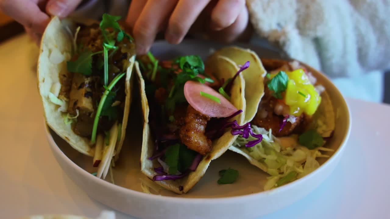 Pige tager taco fra skål med tre mexicanske valgmuligheder.