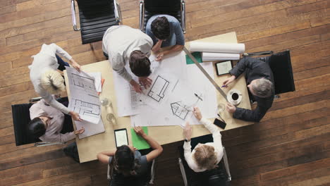 vista superior de personas de negocios que se reúnen alrededor de la mesa de la sala de juntas discutiendo planes arquitectónicos para un nuevo espacio de oficina compartido sostenible