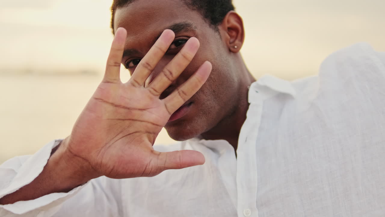 Young Black Man Reveals Face from Behind Hand in Golden Light